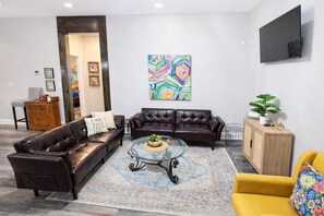 A living room with two leather sofas, a glass coffee table, a patterned rug, a wooden cabinet, and a TV mounted on the wall. - Nashville Escape - Sleeps 8 - Minutes to Broadway (Nashville)