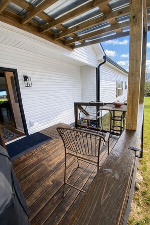 A covered patio with a wooden deck, metal chairs, a table, and a potted plant. - Nashville Escape - Sleeps 8 - Minutes to Broadway (Nashville)