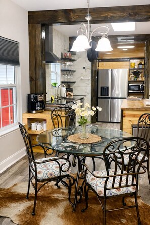 A dining area with a glass table, metal chairs, a vase with flowers, and a cowhide rug. - Nashville Escape - Sleeps 8 - Minutes to Broadway (Nashville)