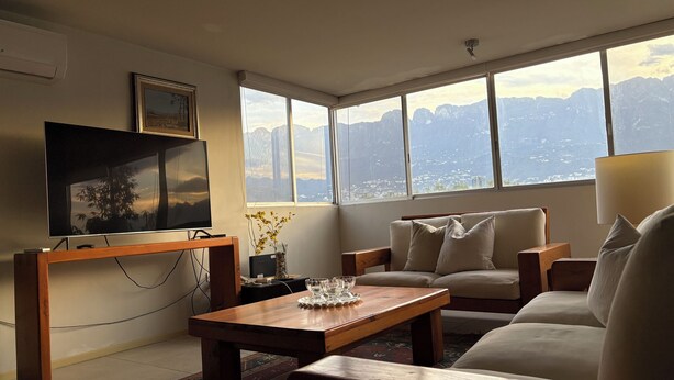 A living room with a TV, a wooden coffee table, a sofa, and a view of mountains through large windows. - Apartment in San Pedro Super Central and Safe Zone (San Pedro Garza García)
