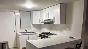 A modern kitchen with white cabinetry, a stainless steel sink, a gas stove, and a small bar stool. - Apartment in San Pedro Super Central and Safe Zone (San Pedro Garza García)