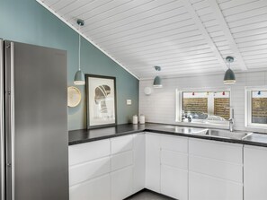 Eine moderne Küche mit weißen Schränken, einem Edelstahl-Kühlschrank, Pendelleuchten und einem Fenster mit Blick auf die Stadt.