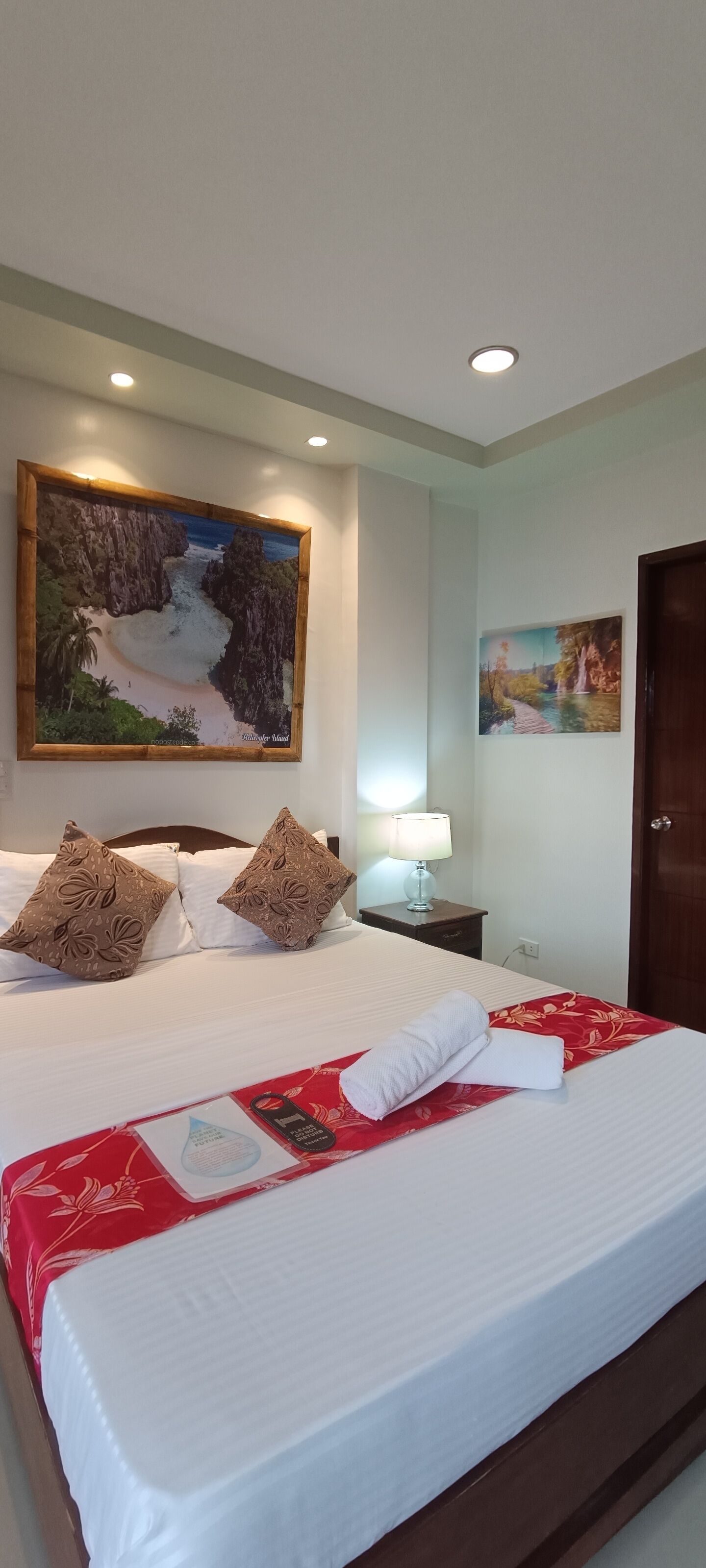 Ein Hotelzimmer mit einem großen Bett, zwei Kissen, einem Nachttisch mit einer Lampe, einem Bild an der Wand und einer Tür.