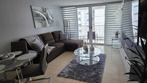 Ein modernes Wohnzimmer mit einer Couch, einem Glastisch und einer Essecke mit Tisch und Stühlen.
