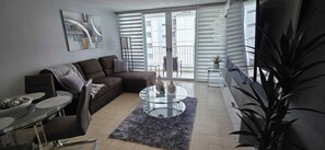 Ein modernes Wohnzimmer mit einer Couch, einem Glastisch und einer Essecke mit Tisch und Stühlen.