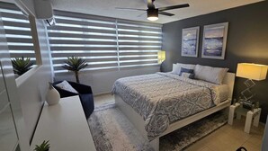Ein Schlafzimmer mit einem Bett, einem Schreibtisch, einem Stuhl, einem Deckenventilator und zwei Wandleuchten.