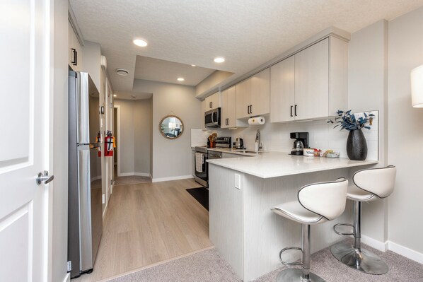 A modern kitchen with stainless steel appliances, a central island with bar stools, and light-colored cabinetry.