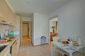 A modern kitchen with a dining area, wooden cabinets, and a small table set for breakfast. - Casa Berna - Balcony Apt with Mountain Views, Lugano, Switzerland (Lugano)