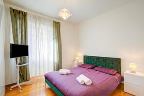 Ein Hotelzimmer mit Bett, Flachbildfernseher, Nachttisch mit Lampe und einem Fenster mit Vorhängen.