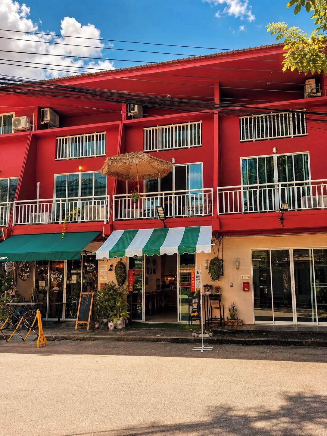 A red building with a green and white striped awning, a balcony with a thatched umbrella, and a storefront with a sign.