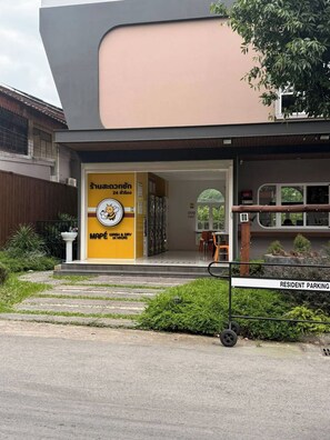 A building with a yellow and grey facade, a resident parking sign, and a small outdoor seating area. - Behome and hostel (Chiang Mai)