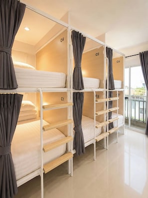 A bunk bed room with curtains, numbered beds, and a view through a glass door. - Behome and hostel (Chiang Mai)