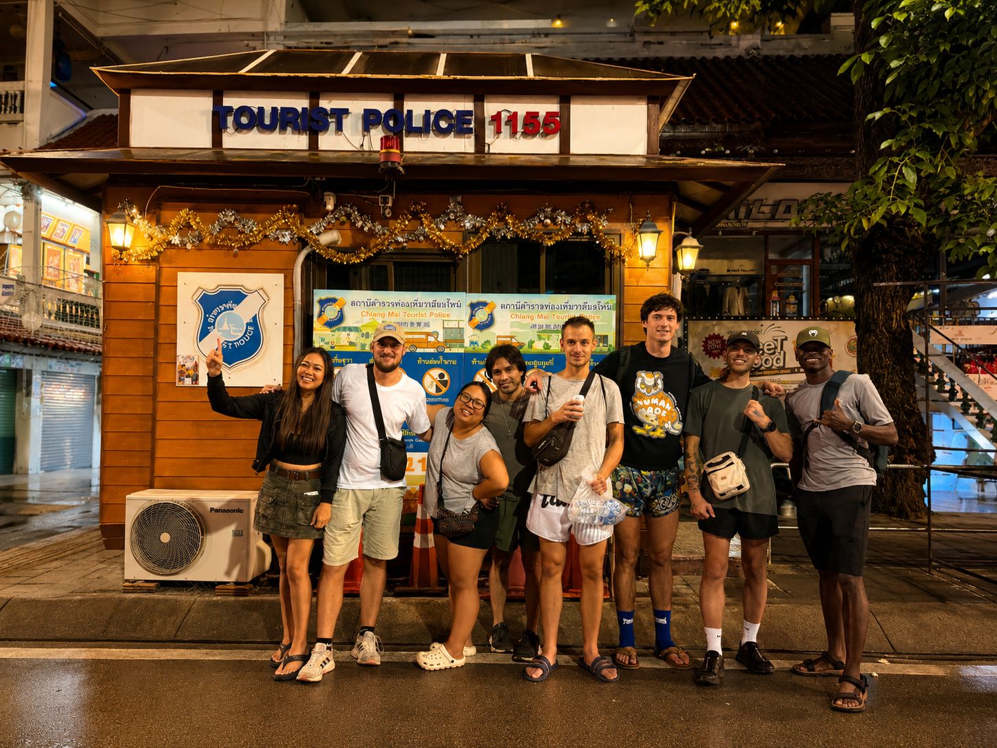 A group of people posing in front of a tourist police booth with a sign and a fan.