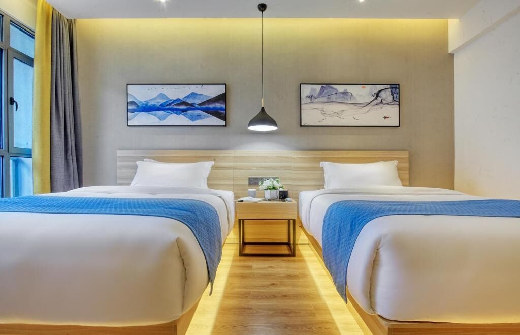 A hotel room with two beds, a nightstand, and artwork on the walls.