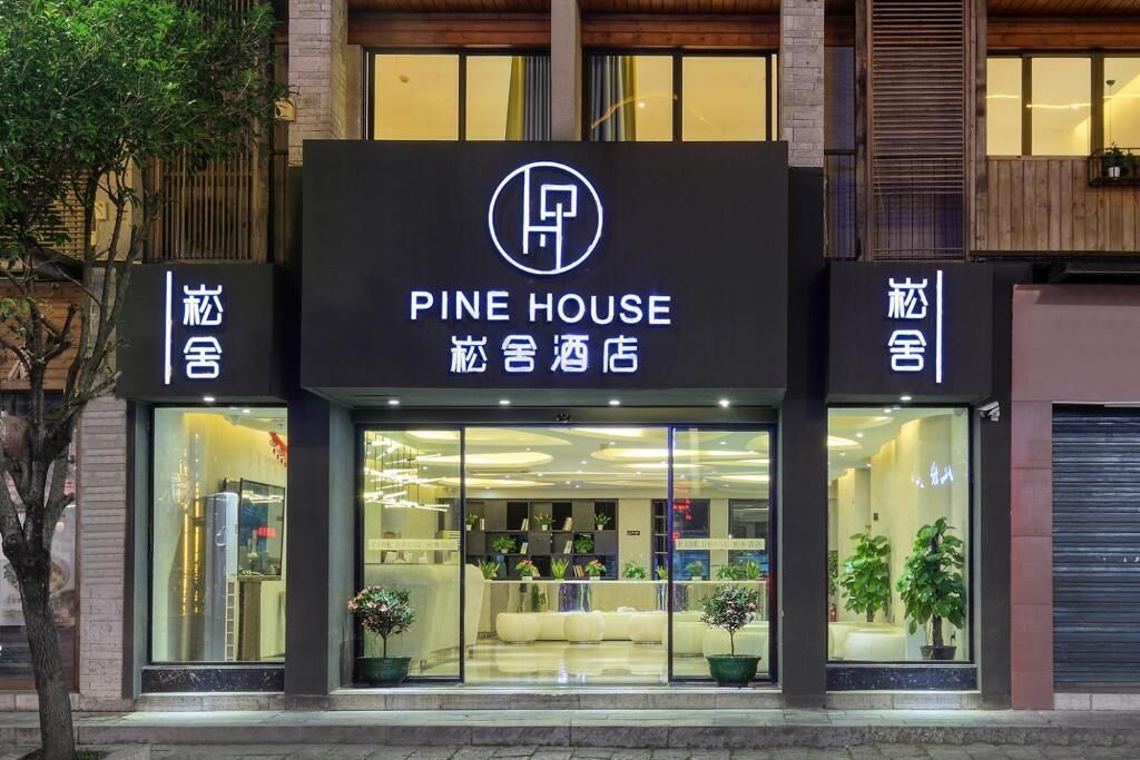 A hotel named 'Pine House' with a modern facade, large glass windows, and potted plants outside.