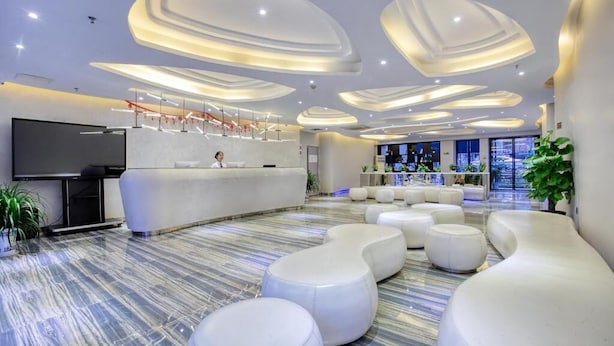 Un vestíbulo moderno con un mostrador de recepción curvo, zona de estar con poufs blancos y un televisor de pantalla plana grande.