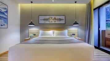 Un dormitorio de hotel moderno con una cama grande, dos lámparas colgantes, un cuadro en la pared y una ventana con cortinas.