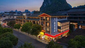 Un hotel con una montaña destacada al fondo, un edificio moderno con ventanas amplias y una entrada bien iluminada.