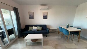Una sala de estar moderna con un sofá, una mesa de centro, una mesa de comedor con sillas y un ventanal corredizo.