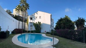Una piscina de borde curvo, rodeada de césped y palmeras.