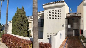 Un edificio con entrada protegida por un portón, un cartel que dice 'BLOQUE 1', y cielo despejado.