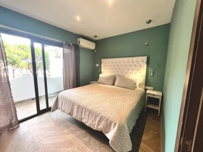 Ein Schlafzimmer mit einem großen Bett, einem Nachttisch, einer Wandlampe und einer Glastür, die zu einem Außenbereich führt.