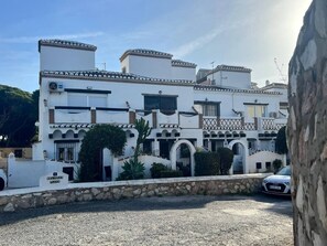 Un immeuble à plusieurs étages, doté d’une façade blanche, de nombreux balcons et d’un mur de pierre à l’avant.