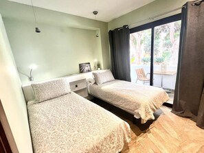Une chambre avec deux lits, une petite table, une chaise et une fenêtre avec des rideaux.