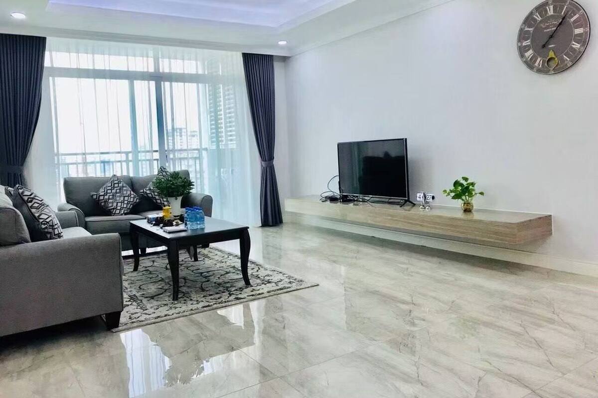 A modern living room with a sofa, coffee table, TV, and a large window with curtains.