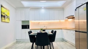 A modern kitchen with white cabinets, a dining table with chairs, a built-in microwave, and a stainless steel refrigerator. - AUREA  (Phnom Penh)