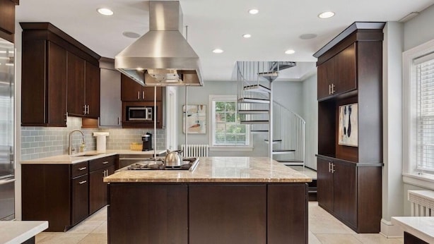 Una cocina moderna con armarios de madera oscura, una isla central, electrodomésticos de acero inoxidable y una escalera en espiral.
