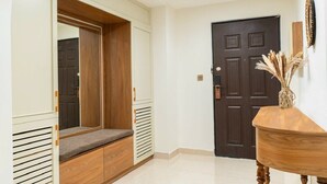 Un couloir avec un banc en bois, une porte sombre et une console en bois sur laquelle est posé un vase.