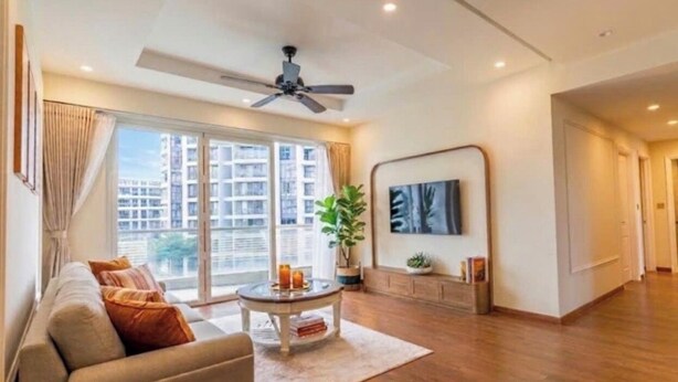 Un salon moderne avec un canapé, une table basse, un ventilateur de plafond et une grande fenêtre donnant sur des immeubles.