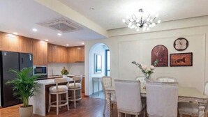 Une cuisine moderne avec des meubles en bois, un îlot central et un coin repas agrémenté de chaises blanches et d’un lustre.