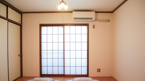 Una habitación con dos camas, un equipo de aire acondicionado, una puerta corredera con diseño de celosía y una lámpara colgante.