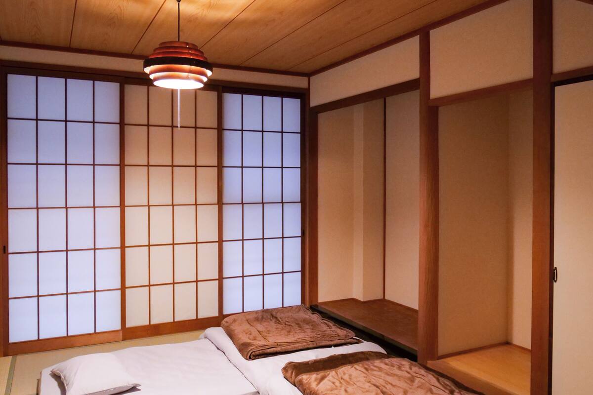 Una tradizionale stanza giapponese con pavimento in tatami, un basso letto di legno con cuscini, una porta scorrevole e un lampadario.