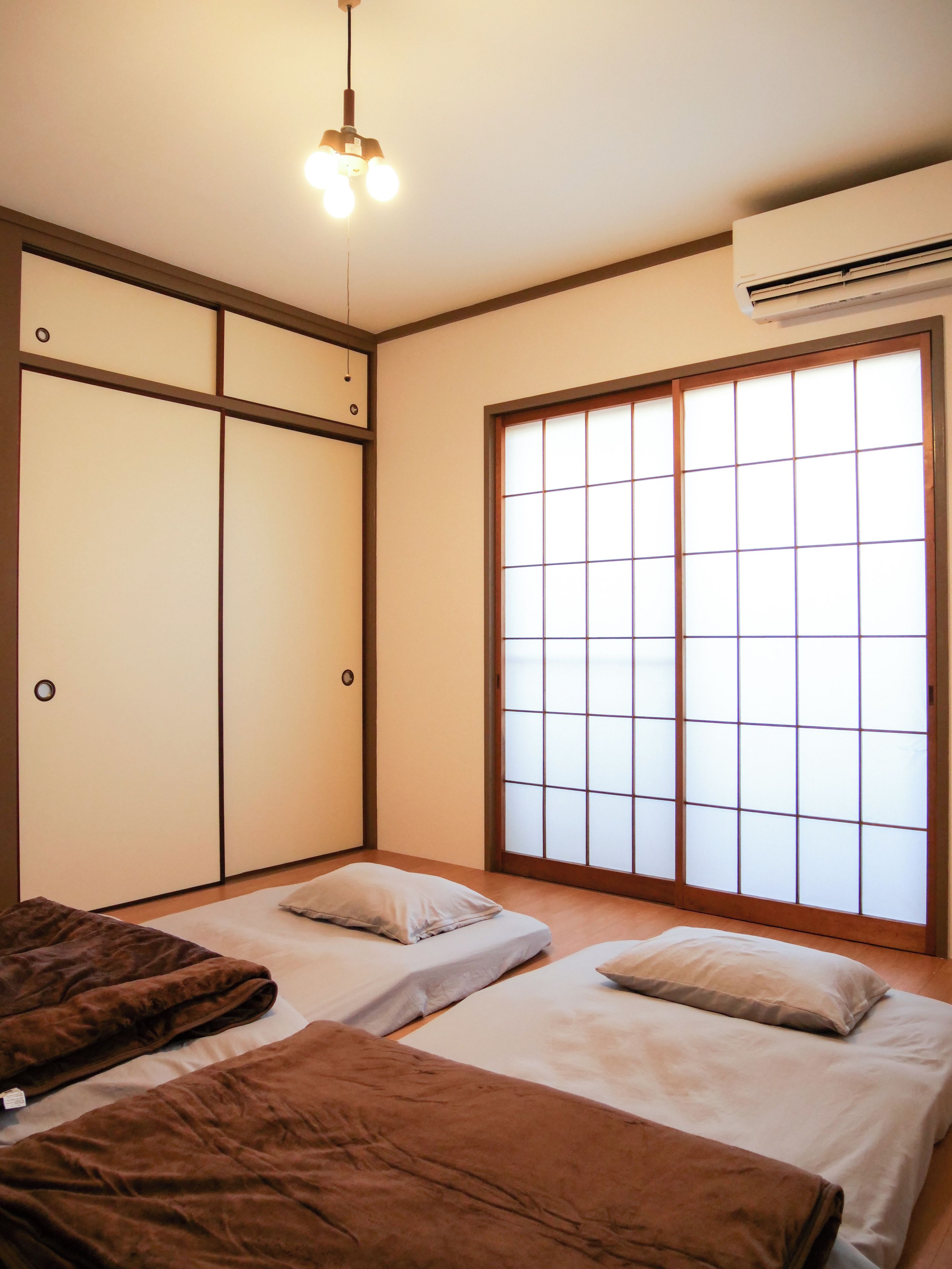 A room with two beds, a sliding shoji screen door, an air conditioning unit, and a hanging light fixture.