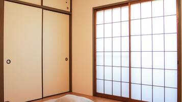 Una habitación con dos camas, una puerta corredera con celosías tipo shoji, un equipo de aire acondicionado y una lámpara colgante.
