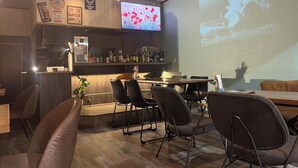 Zona de bar con pantalla de proyección, asientos y barra provista de botellas.
