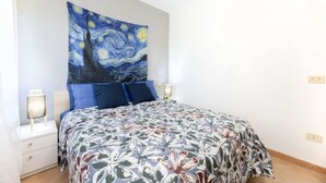 Een slaapkamer met een bed, twee nachtkastjes, een wandtapijt en een bedlamp.