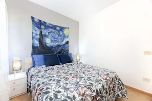 A bedroom with a bed, two bedside tables, a nightstand, a wall tapestry, and a night lamp. - Bilocale Vincent - Goelba (Campo nell'Elba)
