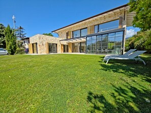 Ein modernes Haus mit Natursteinfassade, großen Glasfenstern und einem gepflegten Rasen.