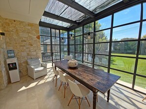 Ein Essbereich mit Steinwand, Wasserspender, Holztisch und weißen Stühlen.