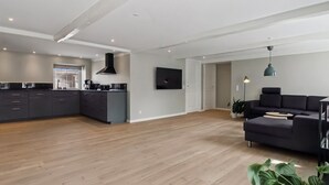 A modern kitchen with dark cabinets and a central island, a living area with a dark sofa and a coffee table, and a large plant in the foreground. - "Farah" - 25km from the sea by Interhome (Skærbæk)