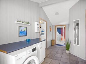 A laundry room with a washing machine, a shelf with glass bottles, and a framed picture on the wall. - "Kiana" - 800m from the sea by Interhome (Hjørring)