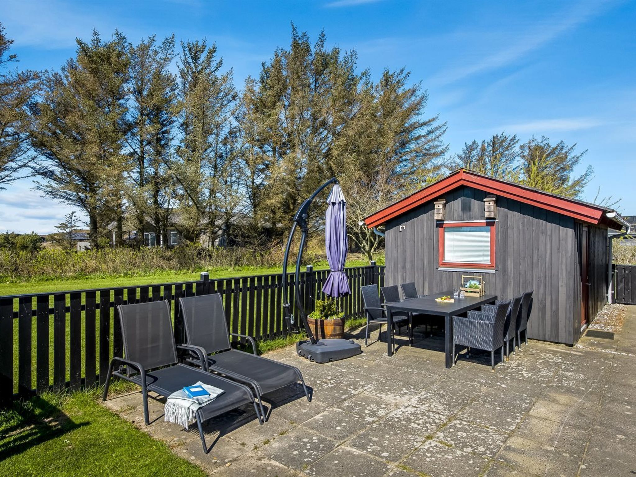 Een terras met buitenmeubilair, een kleine schuur en een houten omheining.