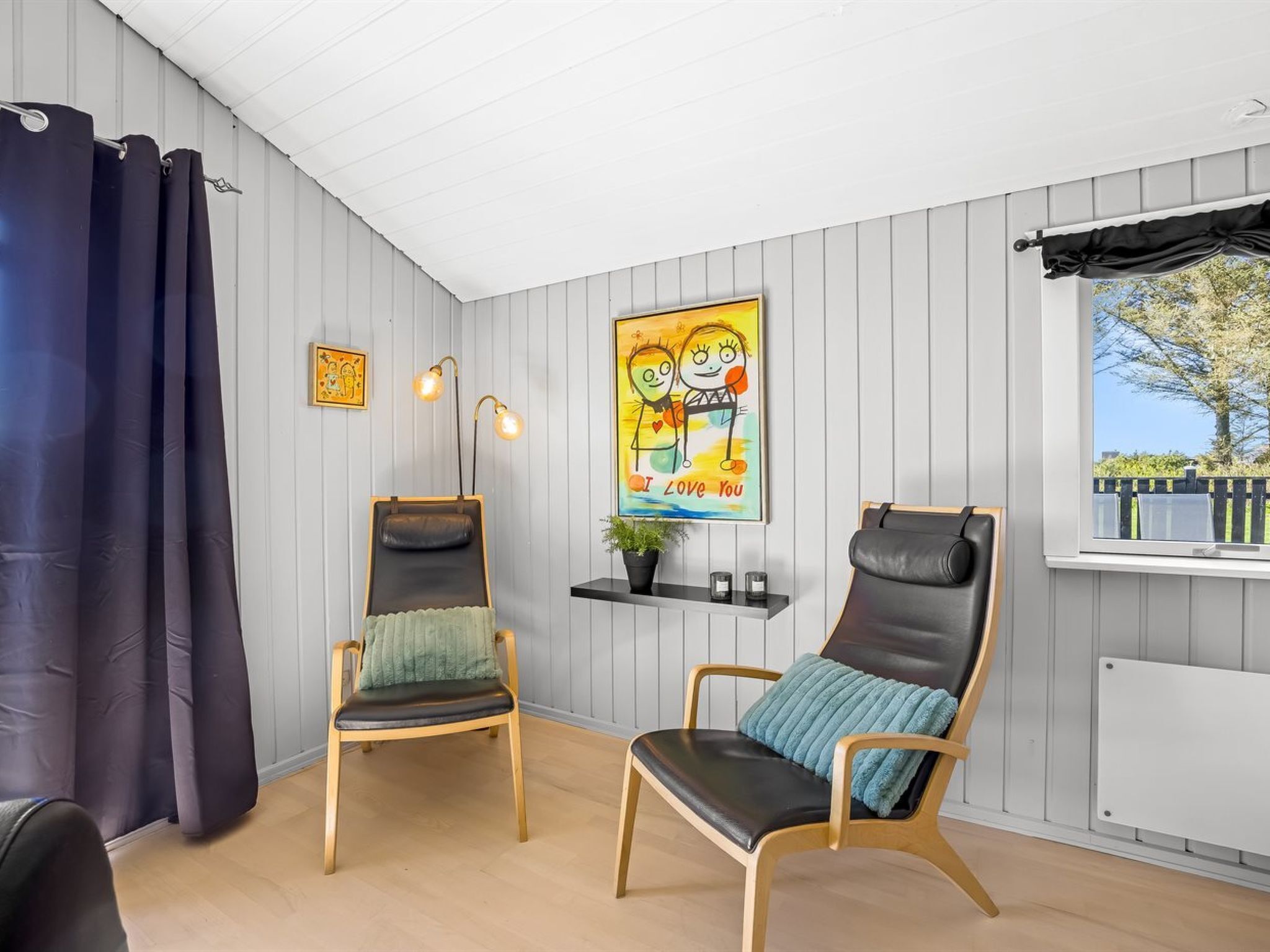 A room with two chairs, a small shelf with a plant, a framed picture, and a window with a view.