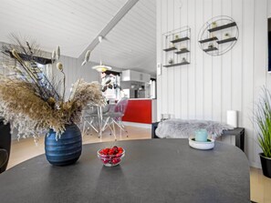 A modern interior with a dining table, a vase with dried flowers, a bowl of cherries, and a kitchen area in the background. - "Kiana" - 800m from the sea by Interhome (Hjørring)