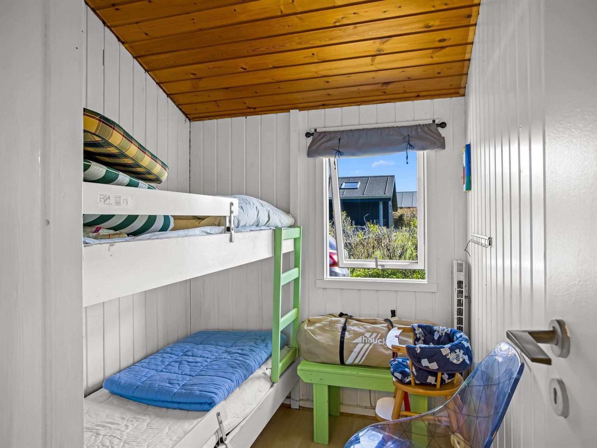 Een slaapkamer met stapelbed, een raam, een groene bank en een tafel met spullen erop.