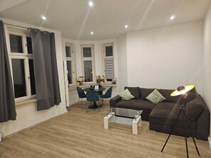 A living room with a brown sofa, a glass coffee table, a dining table with chairs, and a lamp. - Villa Augusta at the Kurpark (Bad Salzuflen)